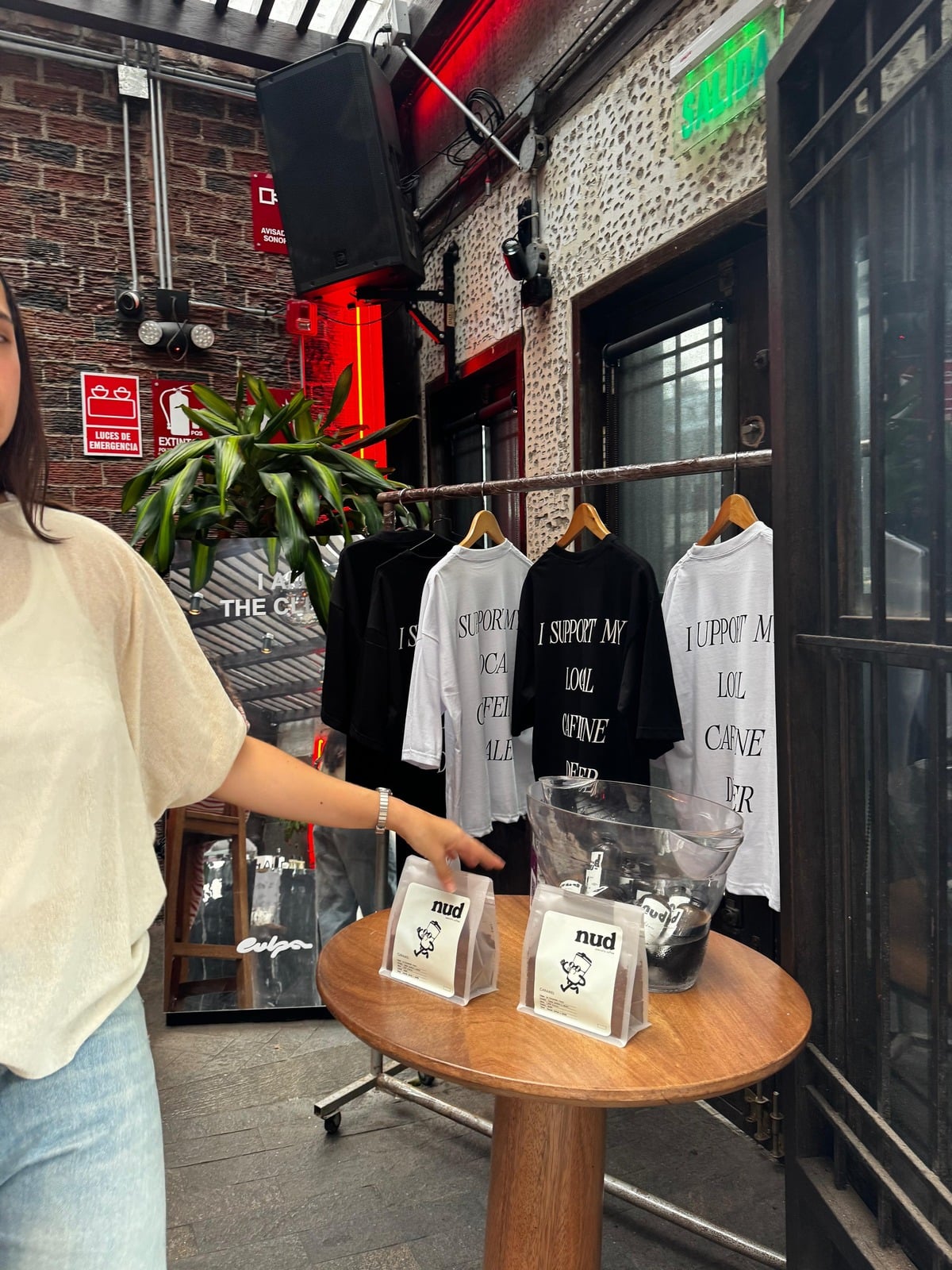 Activación de nud coffee: mesa de madera con botellas y packs de café, y poleras de la marca colgadas detrás