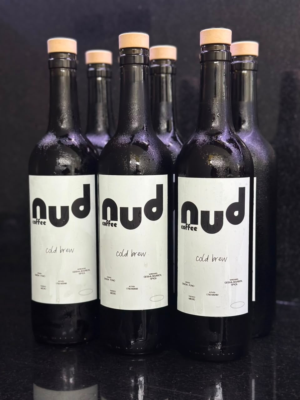 Tres botellas de cold brew de nud coffee con etiqueta blanca sobre fondo oscuro
